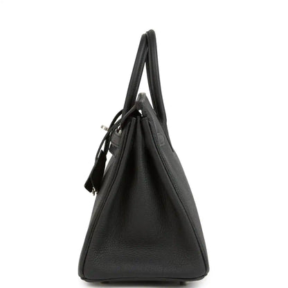Black leather Birkin handbag from side view with top handles and minimal exterior hardware.