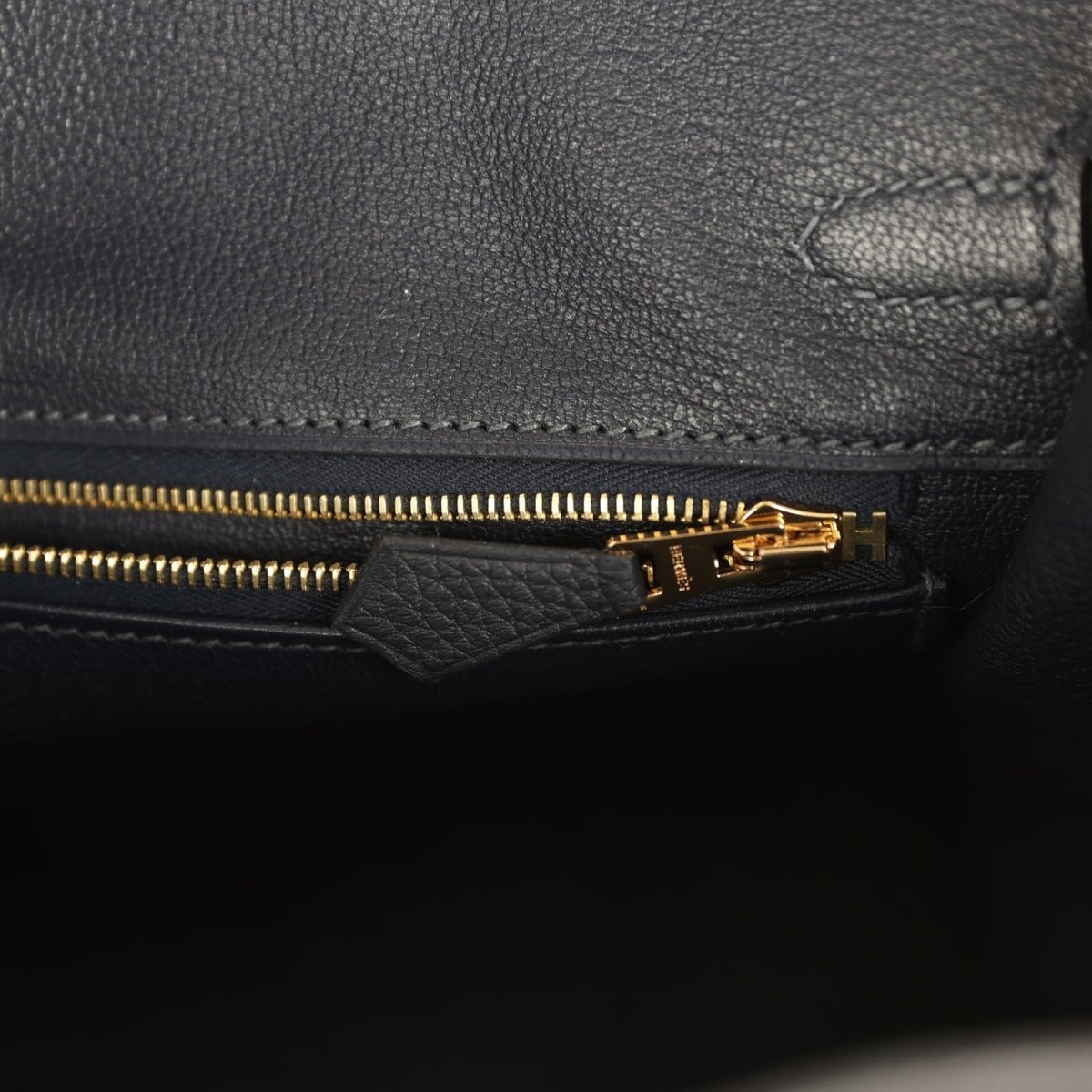 Black leather Birkin-style handbag close-up of gold zipper and turn-lock H detail