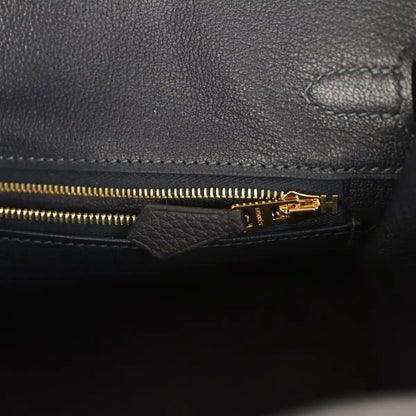 Black leather Birkin-style handbag close-up of gold zipper and turn-lock H detail