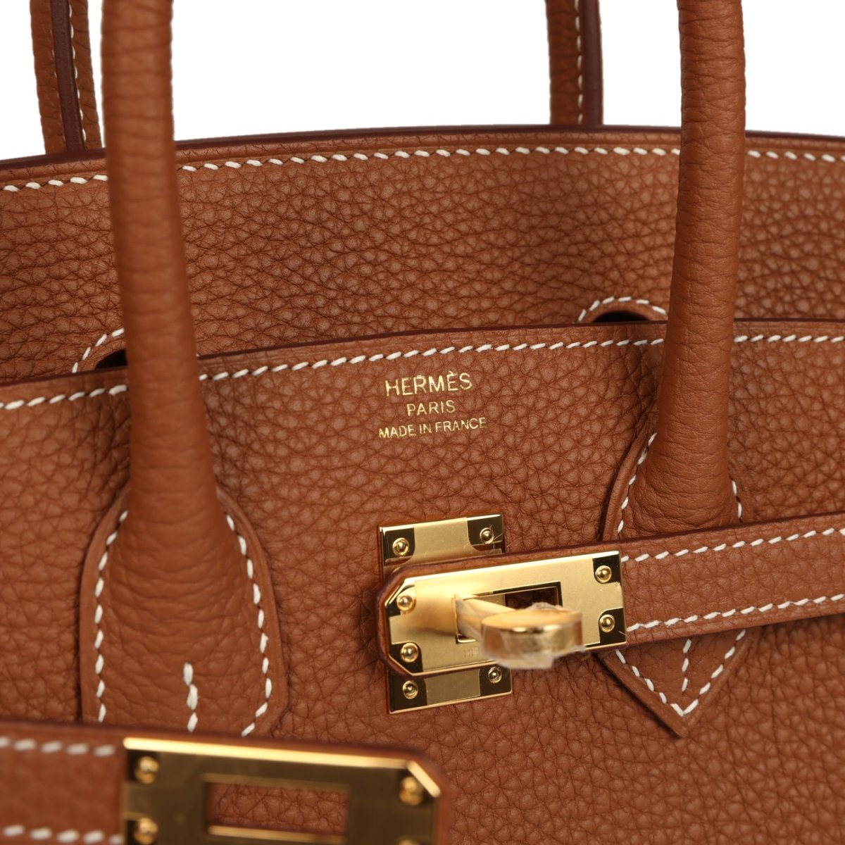 Tan leather handbag close-up showing Hermes Paris stamp, stitching, and gold-tone turnlock.