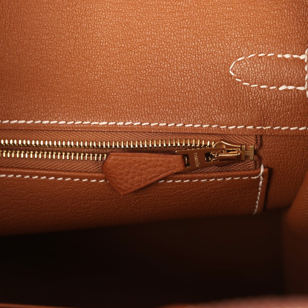 Tan leather handbag close-up of zipper and small pocket with gold-tone pull hardware.