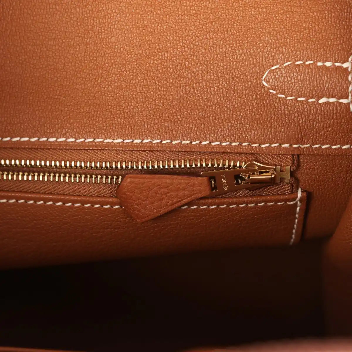 Tan leather handbag close-up of zipper and small pocket with gold-tone pull hardware.
