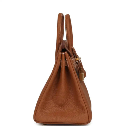 Tan leather handbag viewed from the side, showing top handles and side strap hardware.