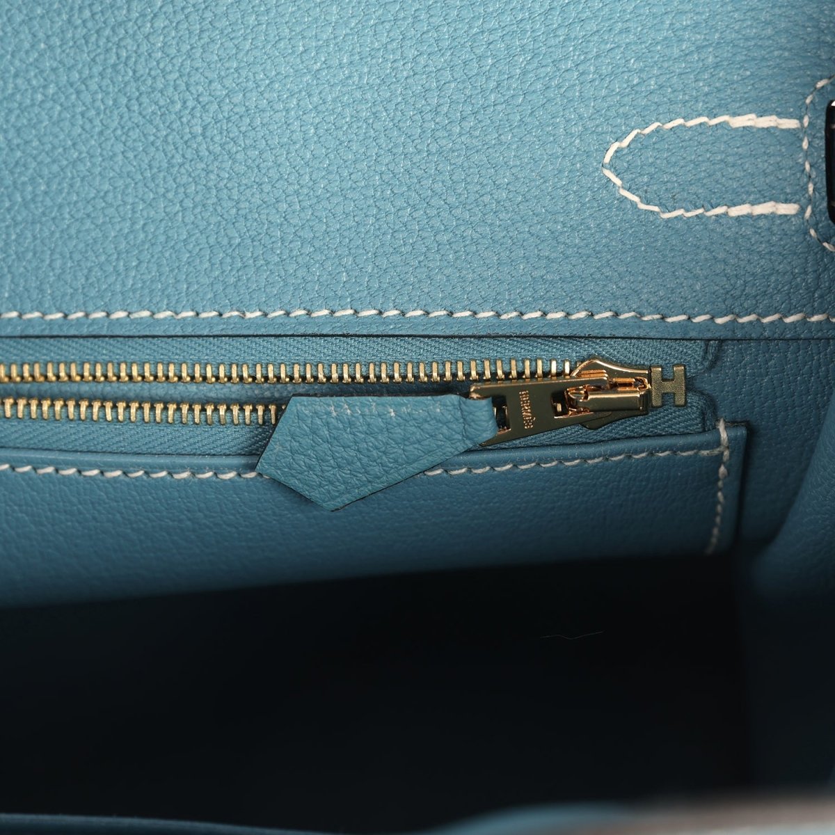 Teal-blue handbag interior zipper with gold-tone pull and small leather tab