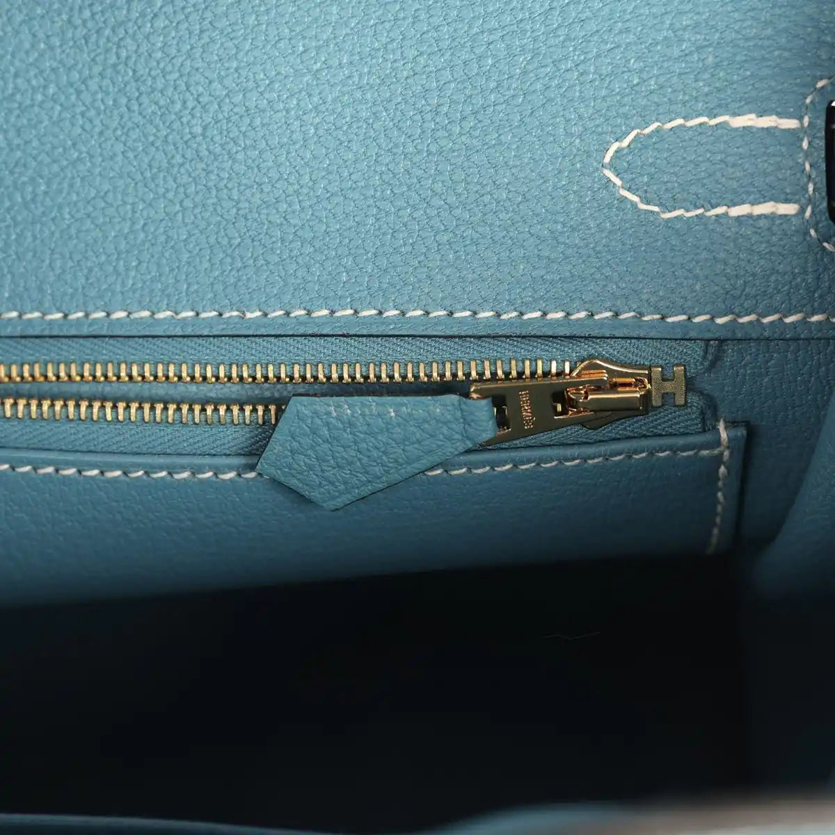 Teal-blue handbag interior zipper with gold-tone pull and small leather tab