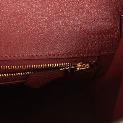 Burgundy leather close-up of gold zipper and stitched compartment edge.