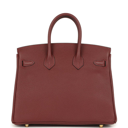 Burgundy leather handbag back panel with hanging straps and gold feet.