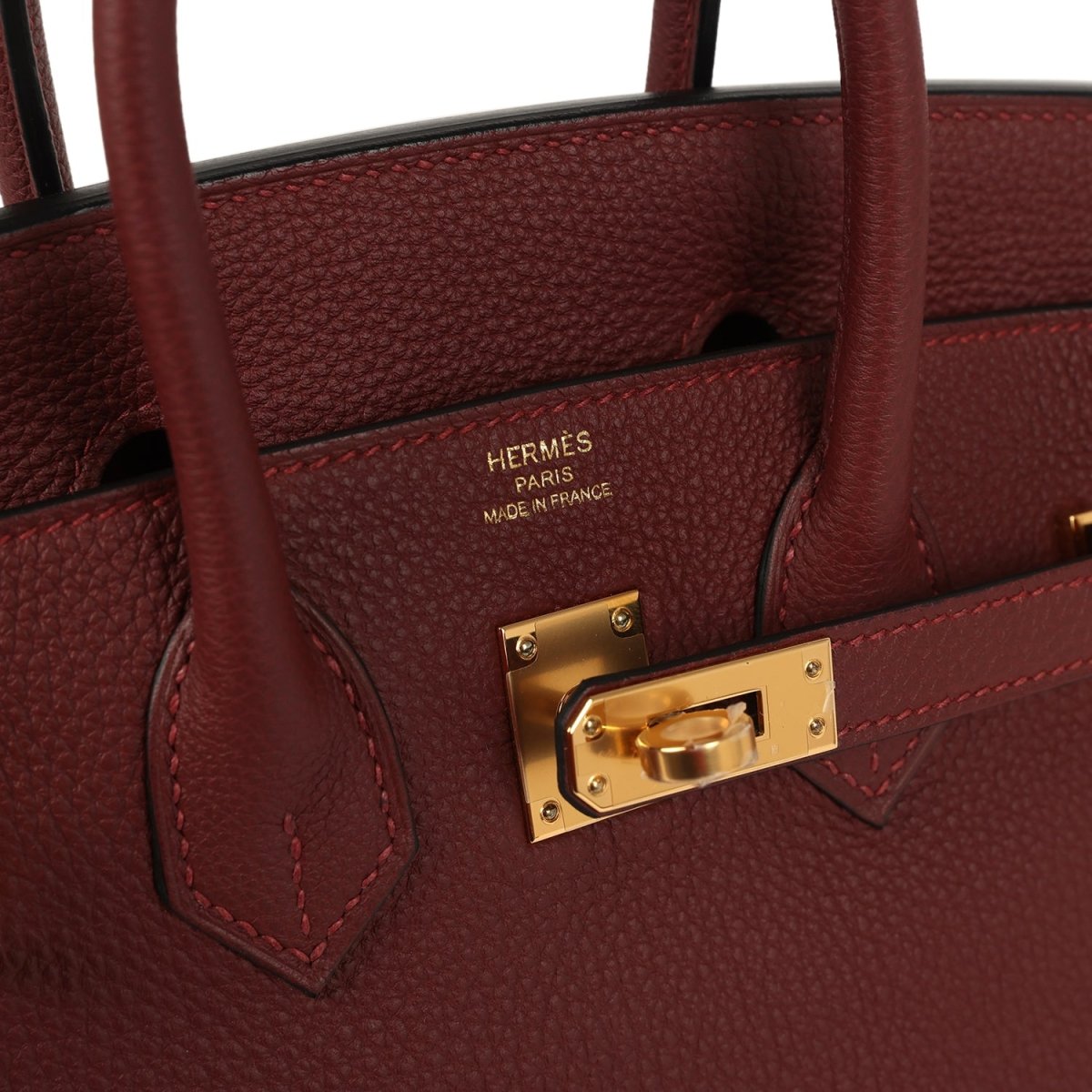 Burgundy leather close-up with gold zipper pull and stitched pocket edge.