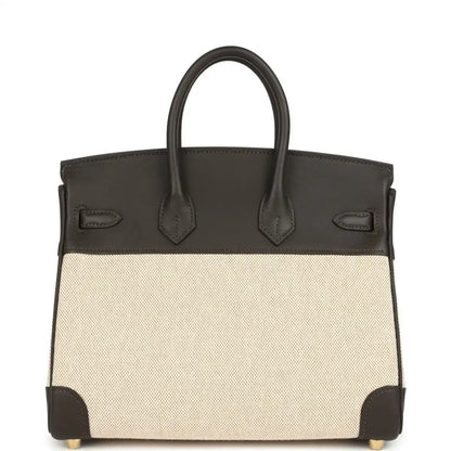Two-tone handbag with dark leather handles, beige canvas body, gold-tone feet and trim