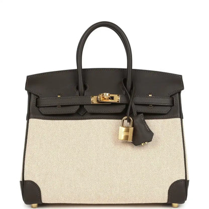 Two-tone handbag with dark leather top handles, beige canvas body, gold-tone lock and front flap