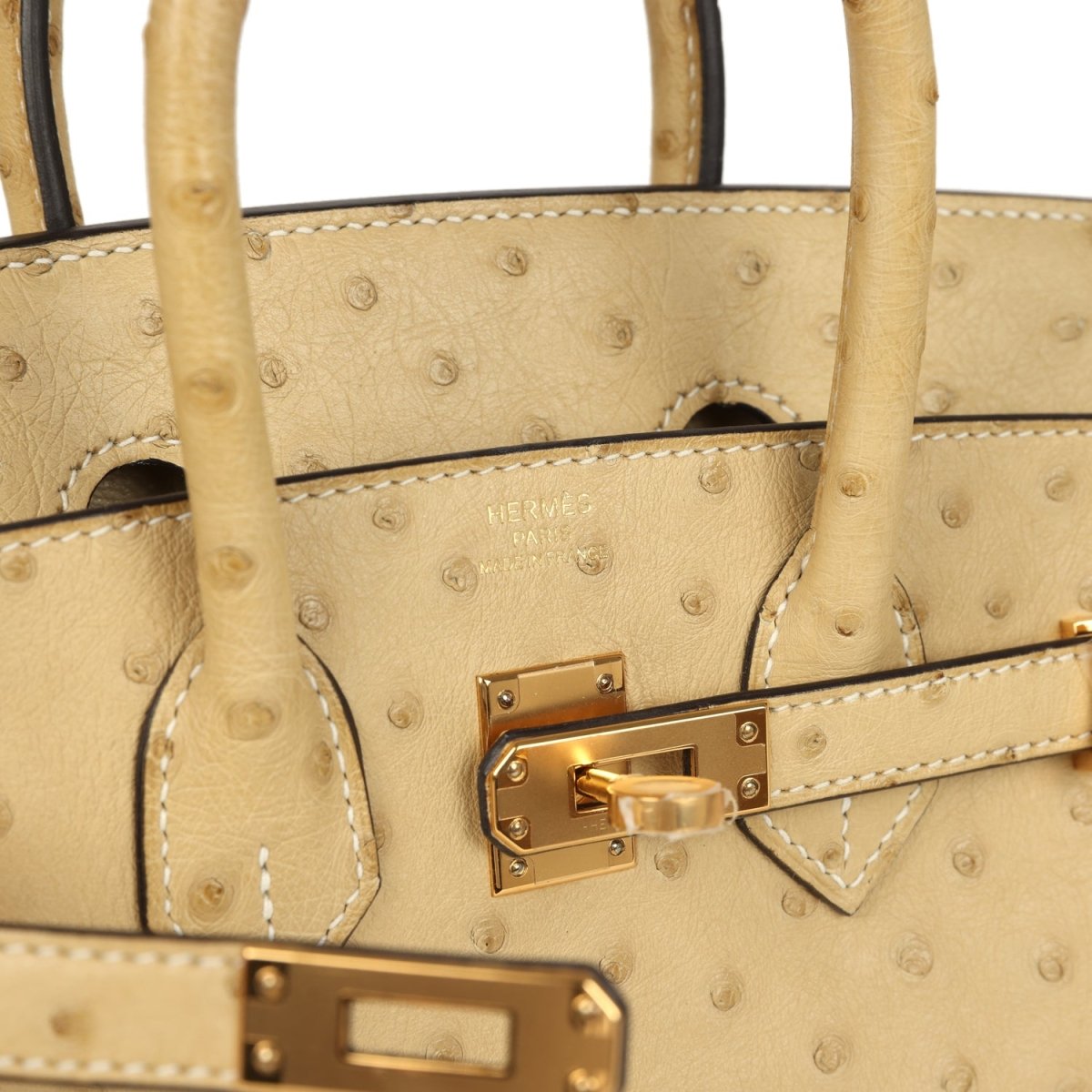 Tan ostrich leather Birkin-style bag close-up with gold-tone front clasp and stitching.