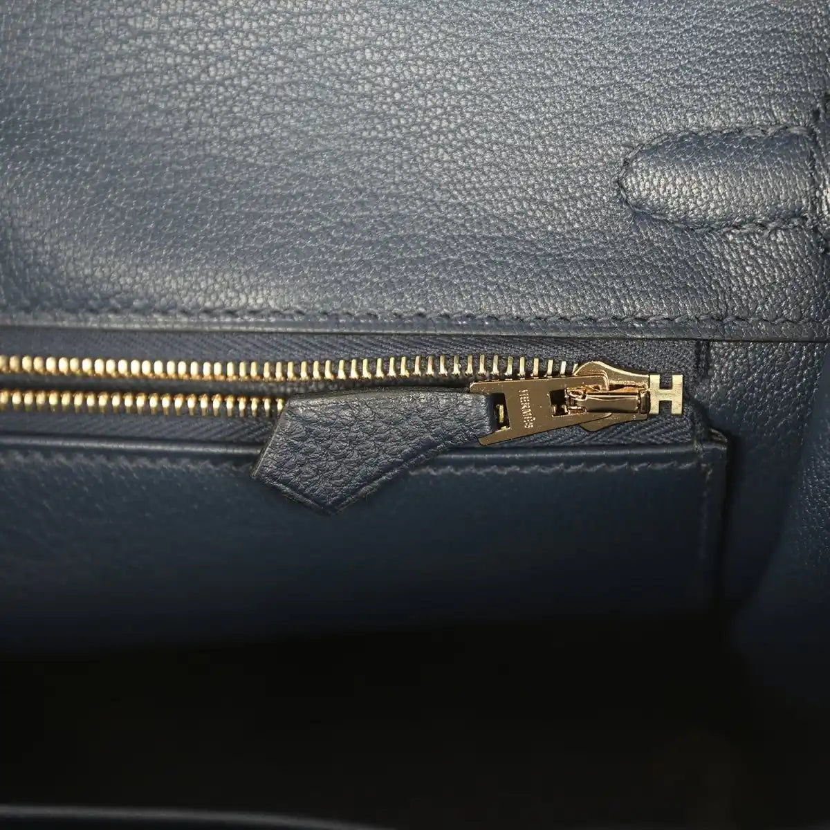 Gold zipper pull on blue Togo leather inner pocket with stamped hardware plate