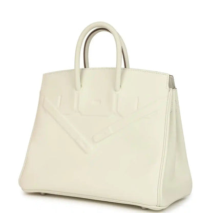 Cream leather handbag with embossed panel and side seam, top handles visible.