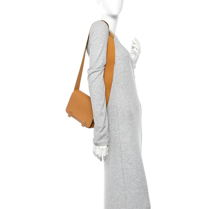 Caramel leather messenger bag worn crossbody with webbing strap and rectangular front hardware