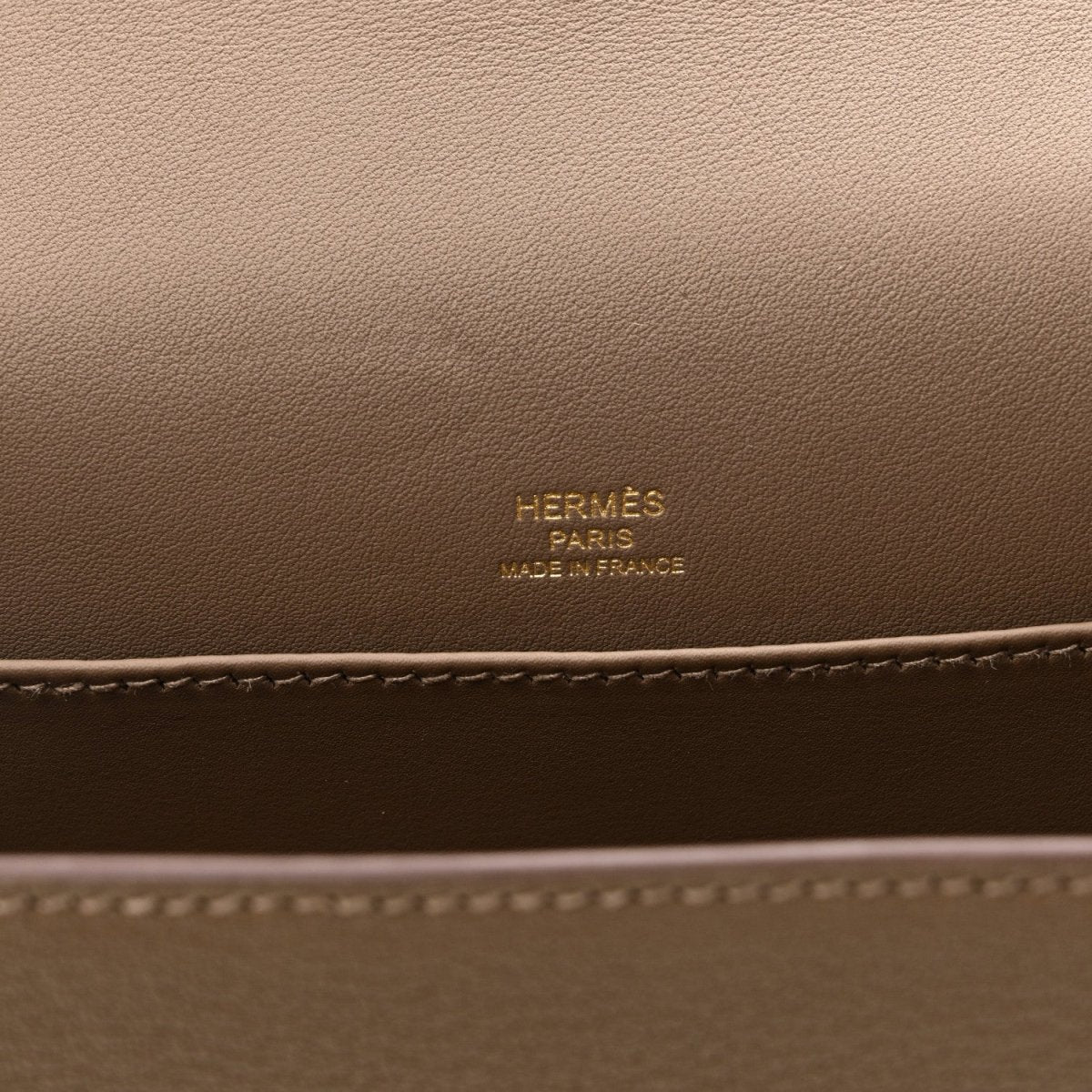 Taupe leather bag panel with embossed brand text and contrast edge stitching