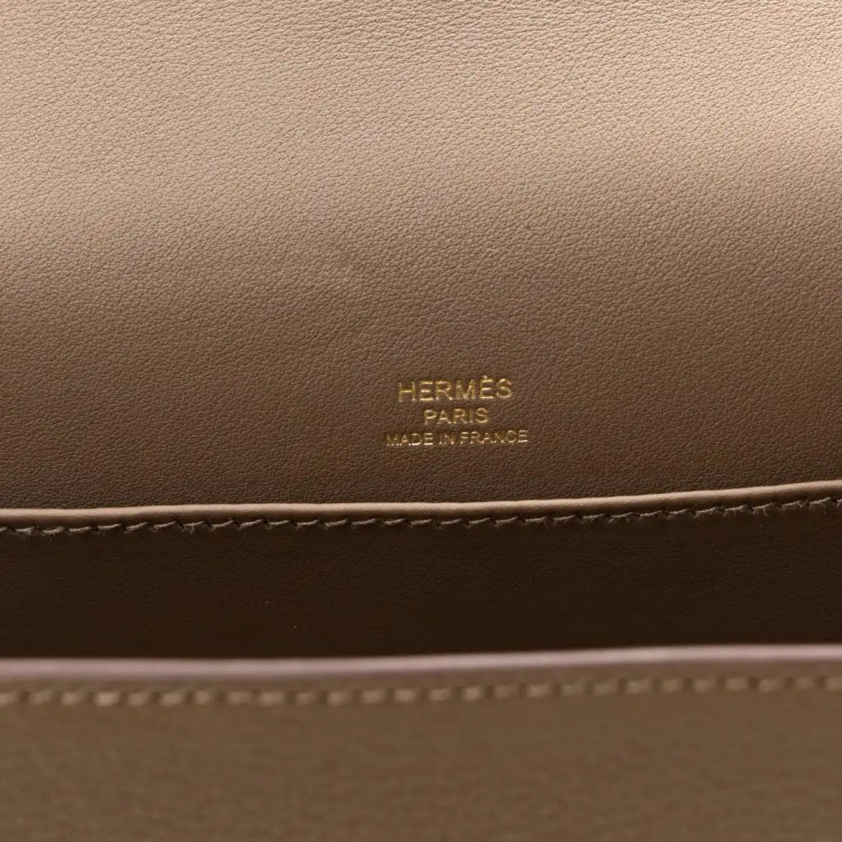Taupe leather bag panel with embossed brand text and contrast edge stitching
