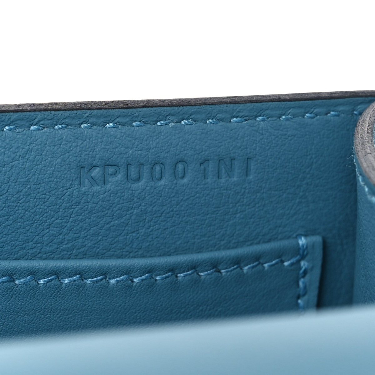 Blue leather bag with embossed code and visible stitched seam detail.