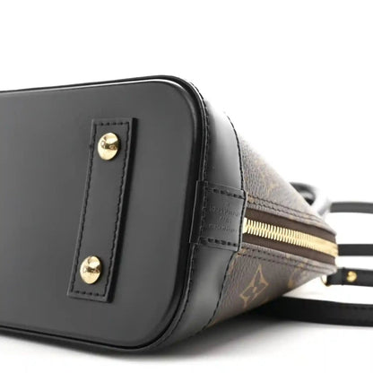 Small monogram tote close-up of black side panel, gold zipper, and strap attachment