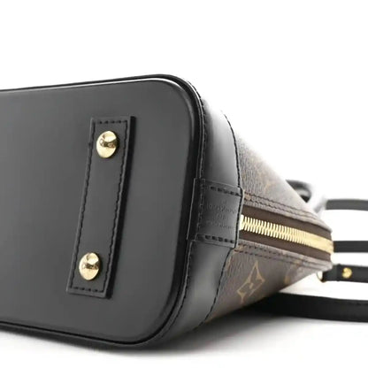 Small monogram tote close-up of black side panel, gold zipper, and strap attachment
