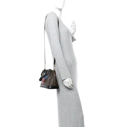 Small monogram tote worn on a person, side view with black strap and top handles
