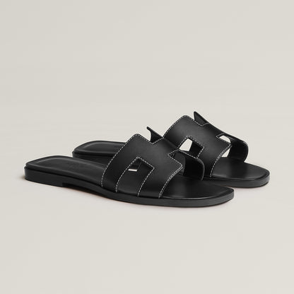 Black leather slide sandal with two wide straps and stitched H-style cutouts