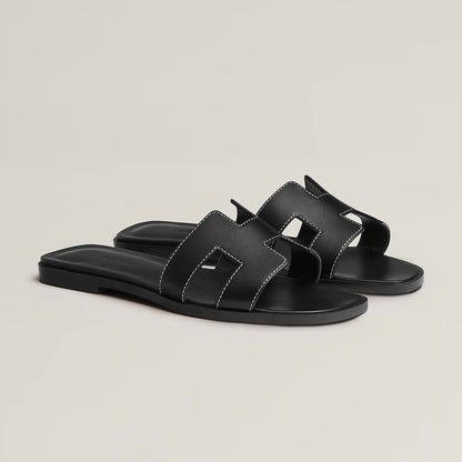 Black leather slide sandal with two wide straps and stitched H-style cutouts