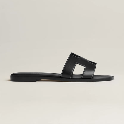 Black leather slide sandal, side view, with wide strap and stitched H-style cutouts