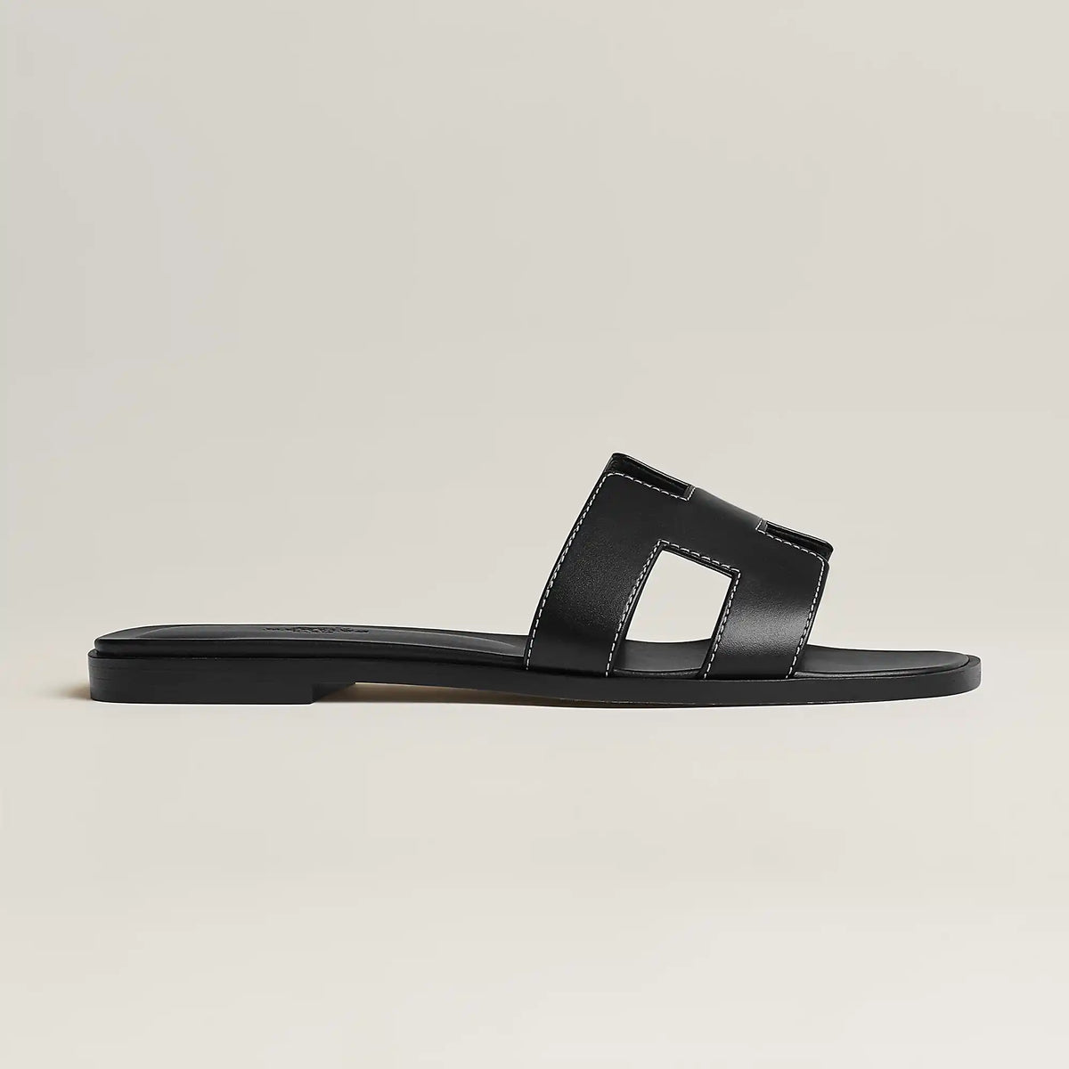 Black leather slide sandal, side view, with wide strap and stitched H-style cutouts