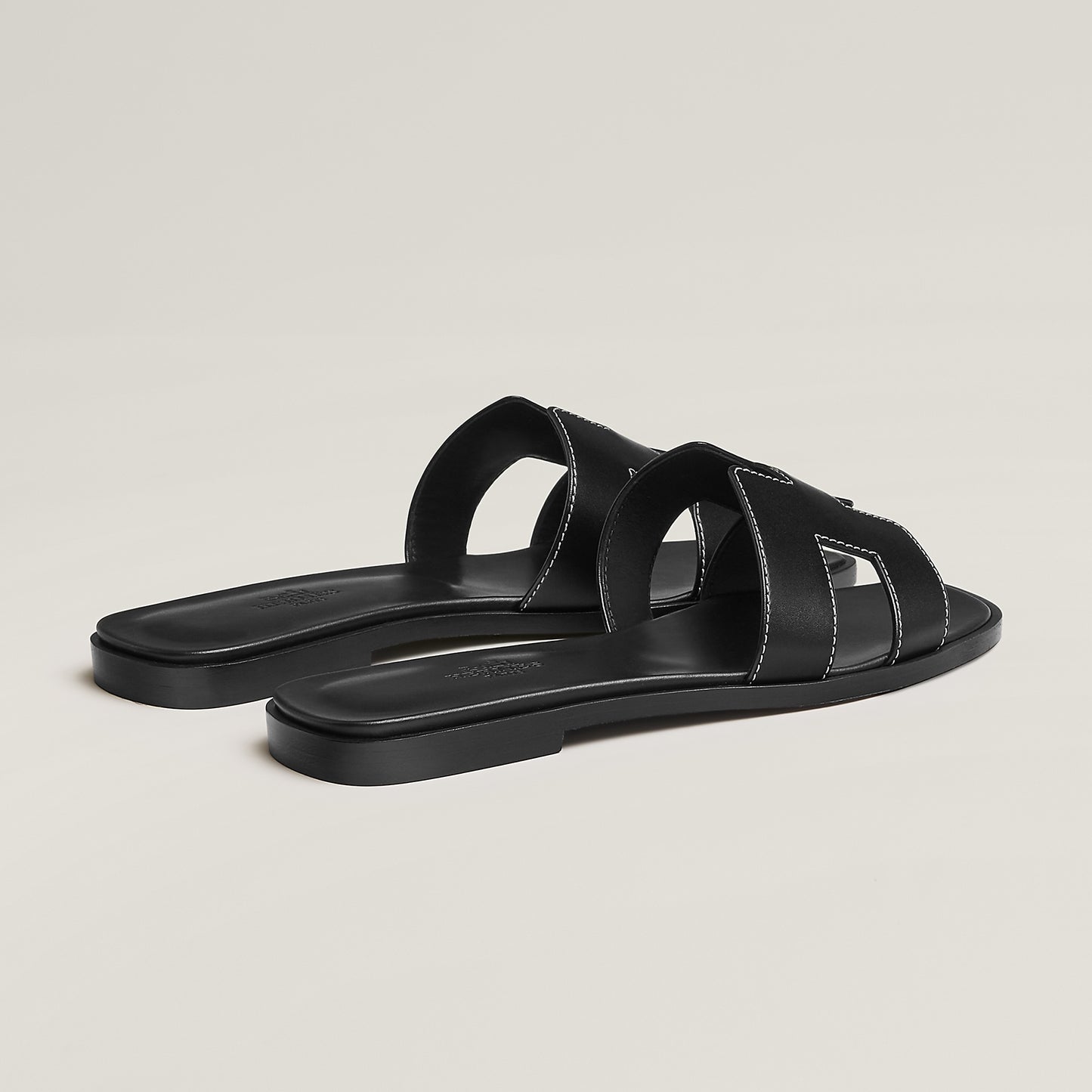 Black leather slide sandal pair, angled view, with wide straps and stitched cutouts
