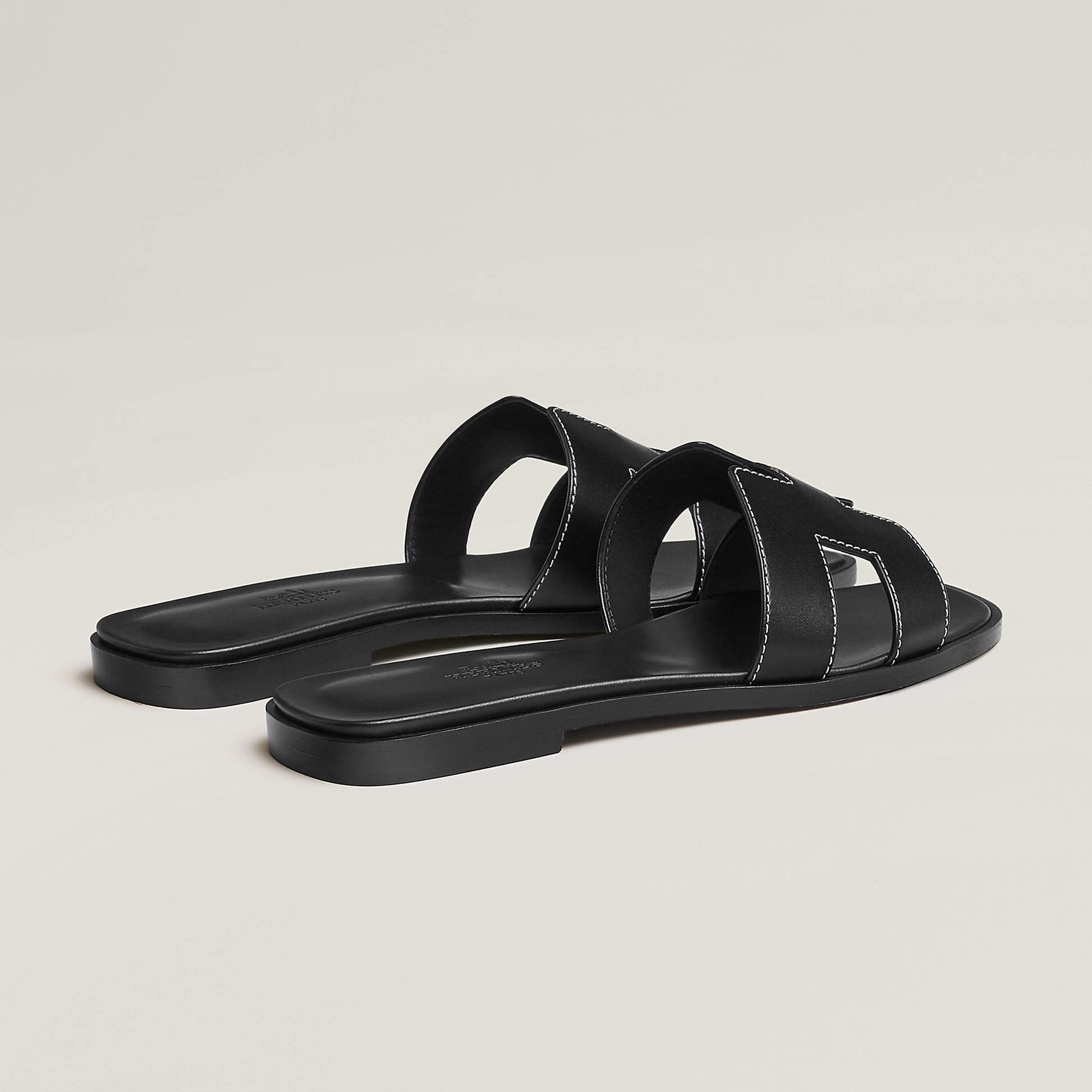 Black leather slide sandal pair, angled view, with wide straps and stitched cutouts