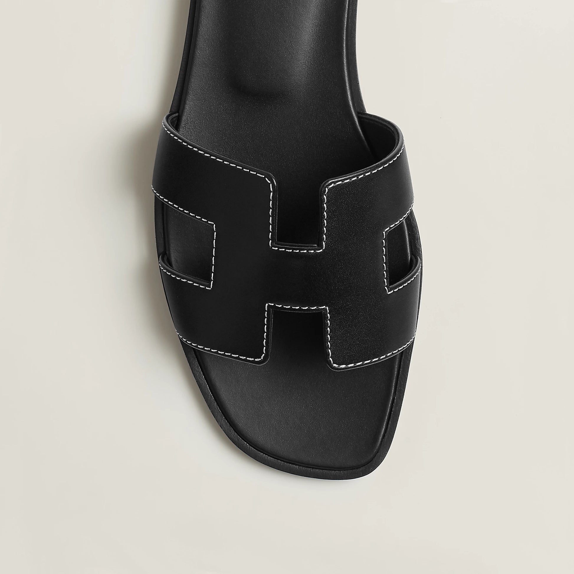 Black leather slide sandal upper close-up with stitched H-style cutouts and open toe