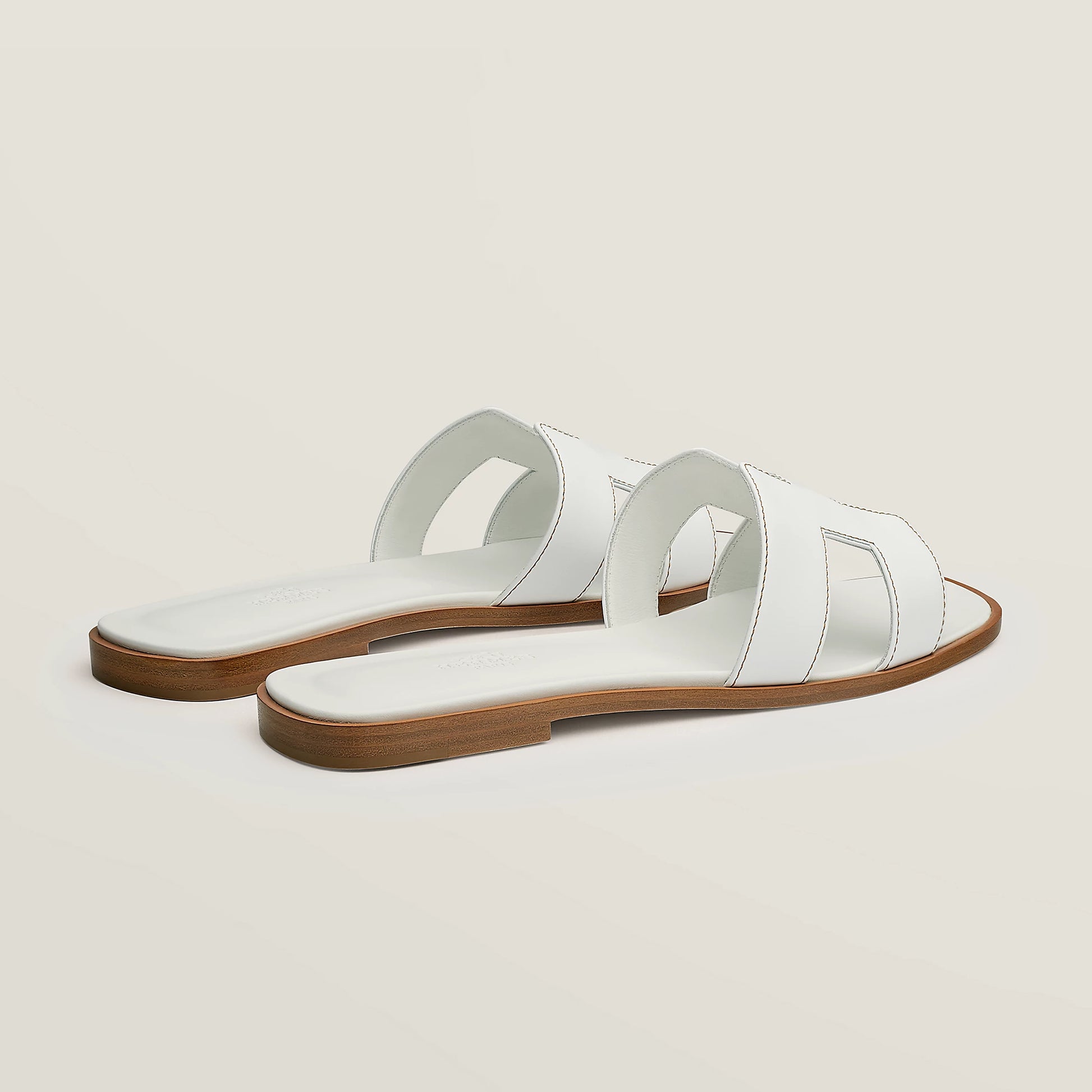 White leather slide sandal pair, angled view, with wide straps and stitched cutouts