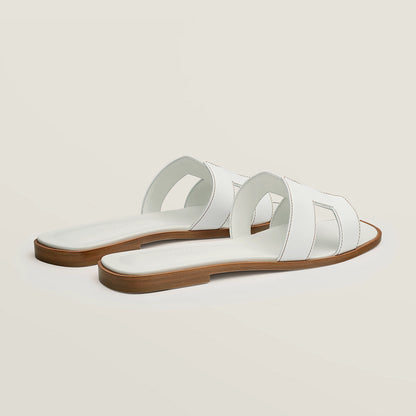 White leather slide sandal pair, angled view, with wide straps and stitched cutouts