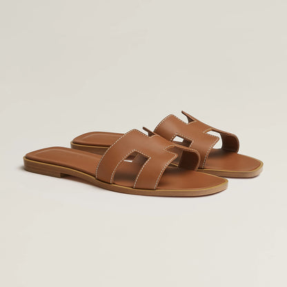 Tan leather slide sandal with two wide straps and stitched H-style cutouts