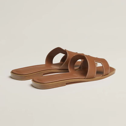 Brown leather slide sandal pair, angled view, with wide straps and stitched cutouts