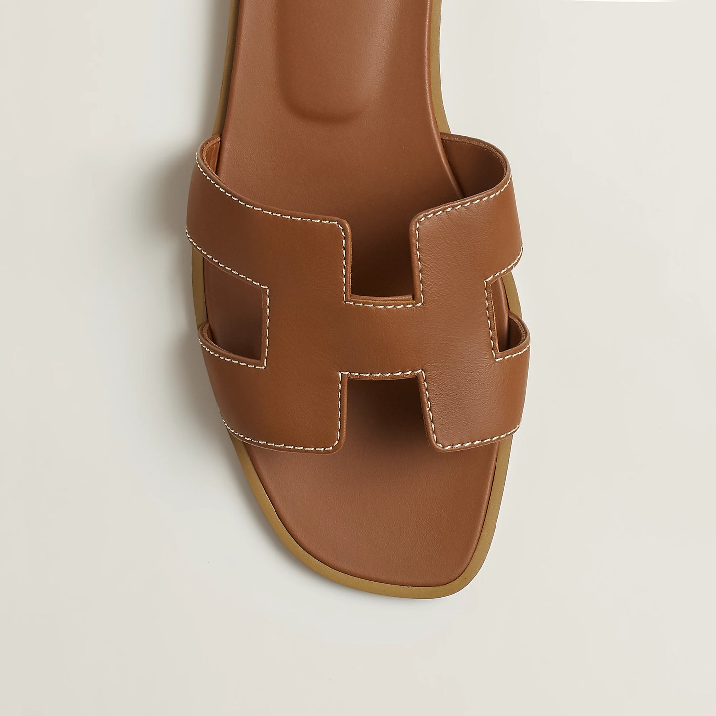 Tan/brown leather slide sandal upper close-up with stitched H-style cutouts and open toe