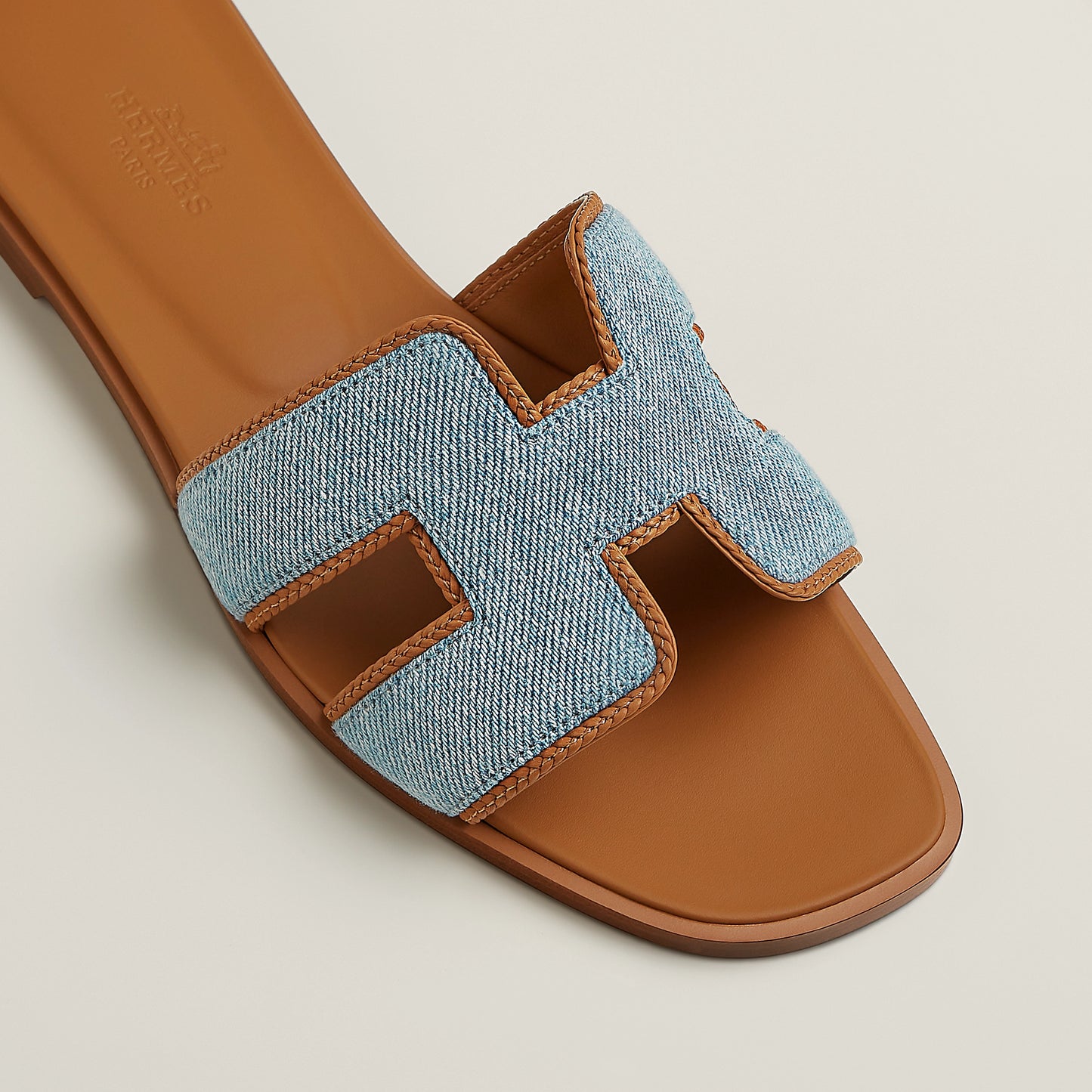 Oran slide sandal close-up: light blue denim upper with tan leather double straps