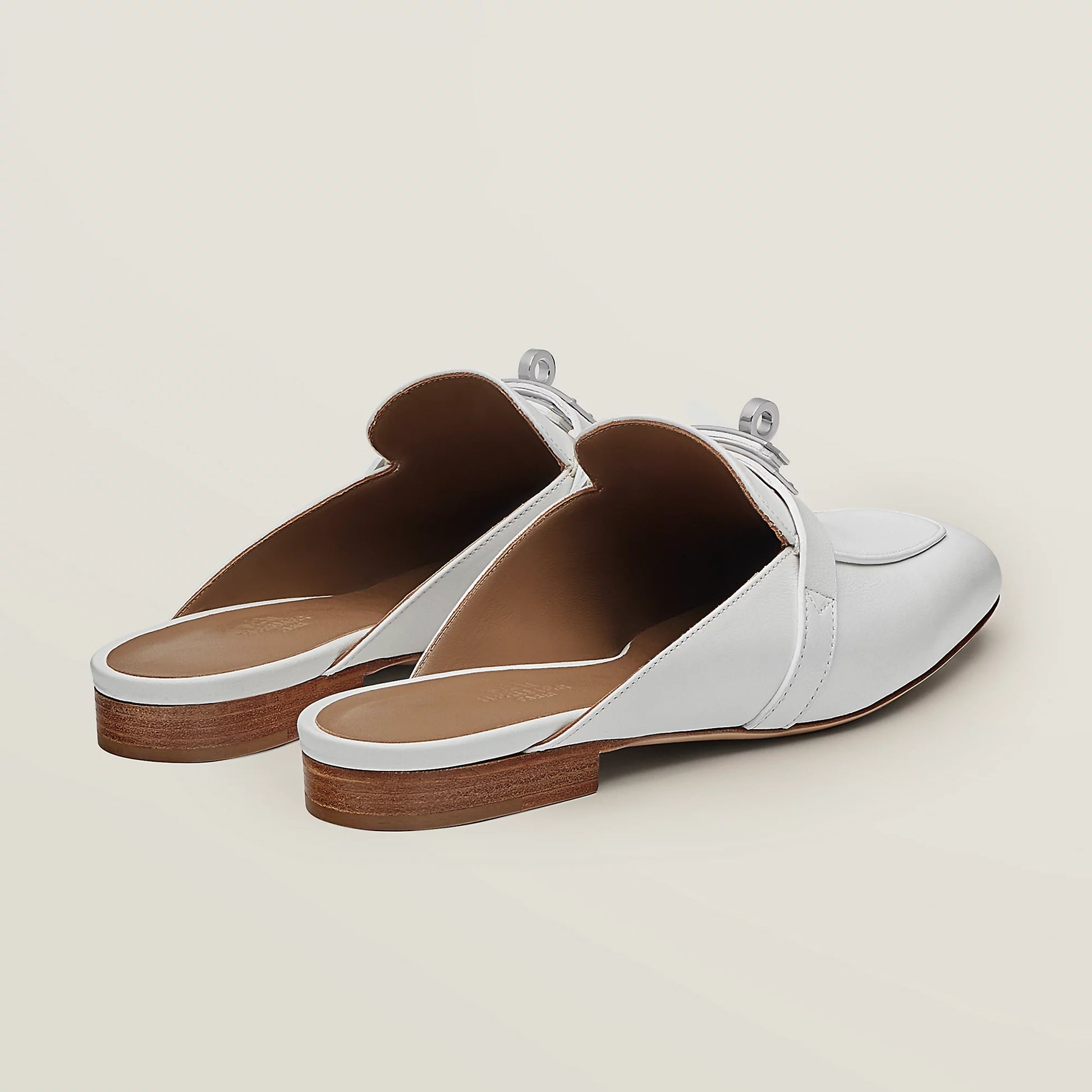 White leather mule slippers with buckle strap, brown insole lining, and low heel