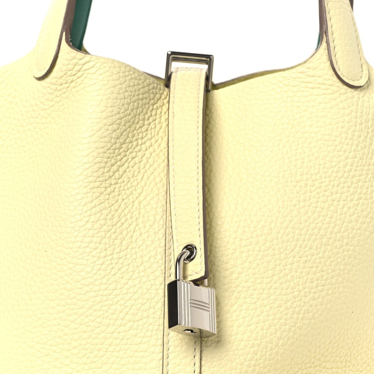 Two-tone leather handbag close-up with metal lock clasp on yellow front and green handle.