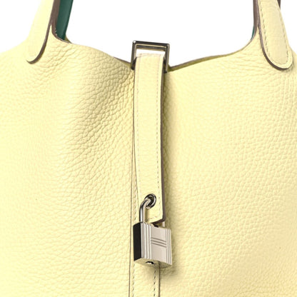 Two-tone leather handbag close-up with metal lock clasp on yellow front and green handle.
