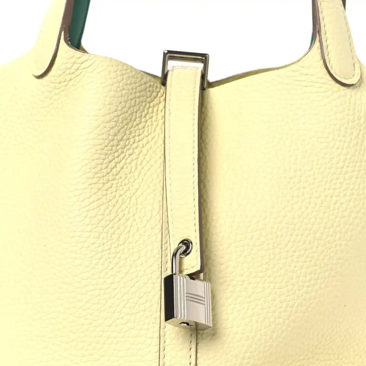 Two-tone leather handbag close-up with metal lock clasp on yellow front and green handle.