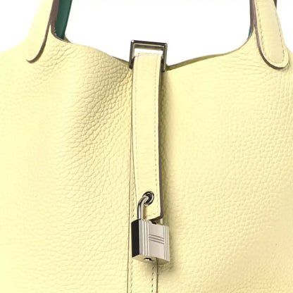 Two-tone leather handbag close-up with metal lock clasp on yellow front and green handle.