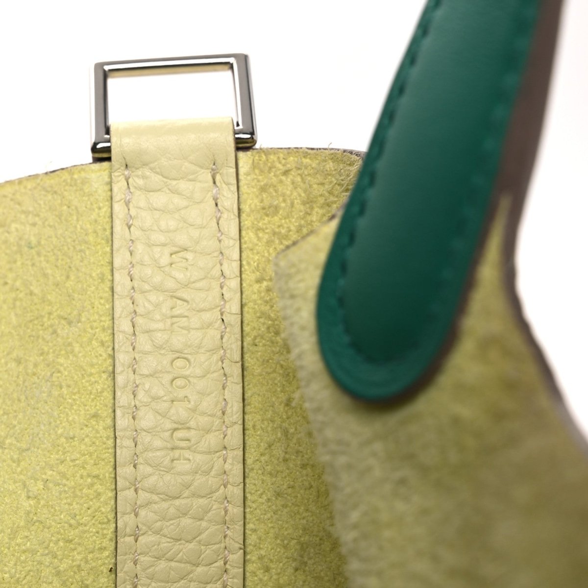 Two-tone handbag close-up: yellow strap attachment with green edge and metal bar clasp.