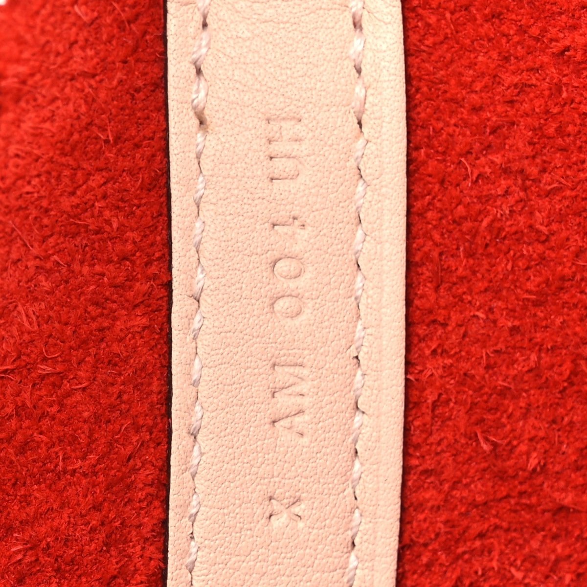 Pale leather strap seam detail on red tote bag.