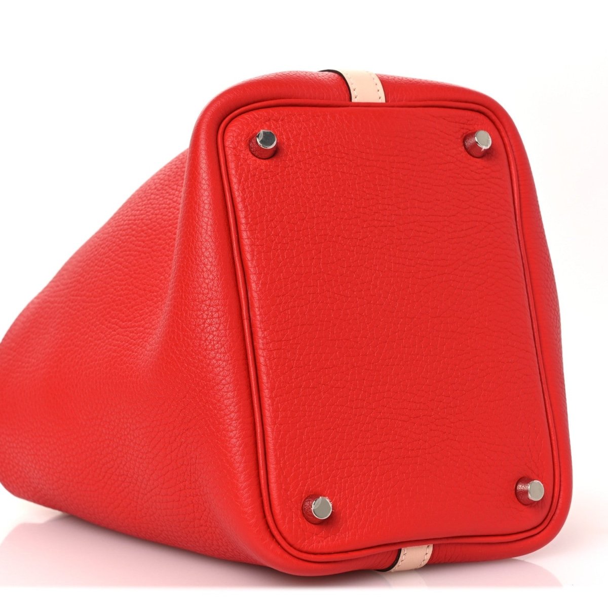 Red pebbled leather tote bag top corner with silver hardware and pale trim strip.