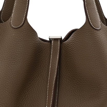 Taupe leather bag front close-up with center lock hardware and contrast edge stitching.
