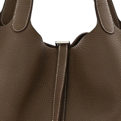 Taupe leather bag front close-up with center lock hardware and contrast edge stitching.
