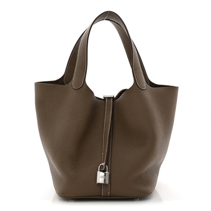 Taupe leather bucket bag with top handles and center lock closure, textured grain.