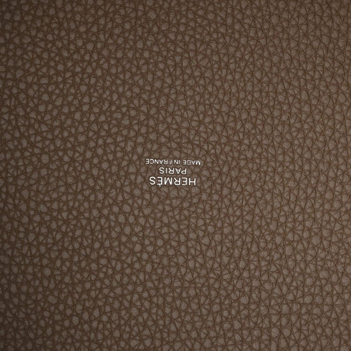 Taupe leather close-up with embossed “HERMES” stamp on textured calfskin.