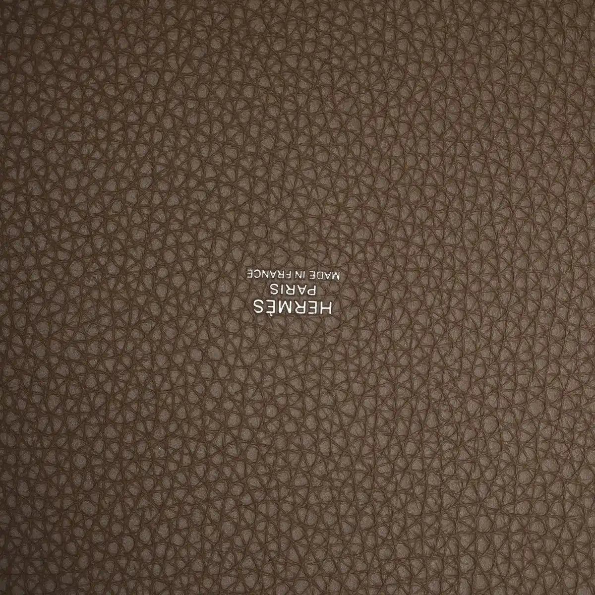 Taupe leather close-up with embossed “HERMES” stamp on textured calfskin.